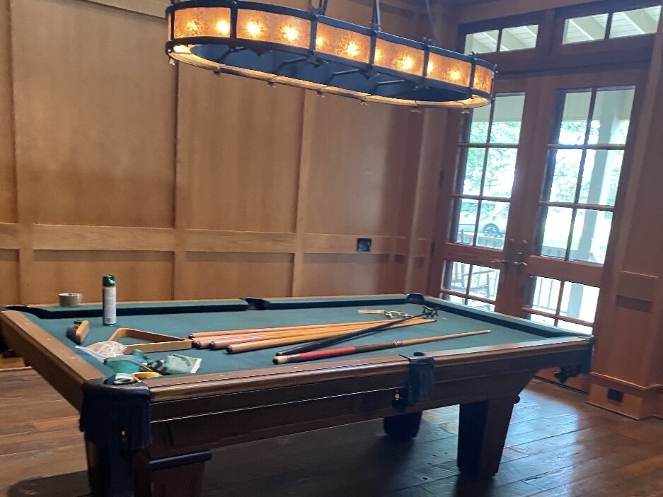 The pool table in the ranch house, cues laid across the felt under a long iron light